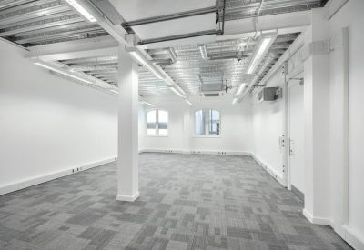 Spacious open-plan office with white walls, exposed ceiling, and grey carpet.