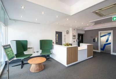 Modern reception area with a white desk, wood panels, and green wingback chairs.