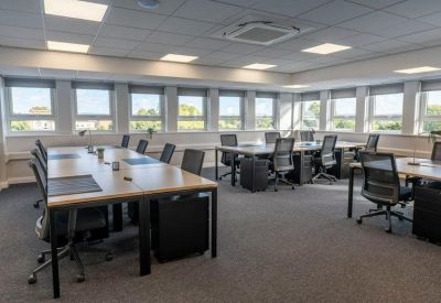 Open-plan office space with rows of modern wooden desks and ergonomic chairs.