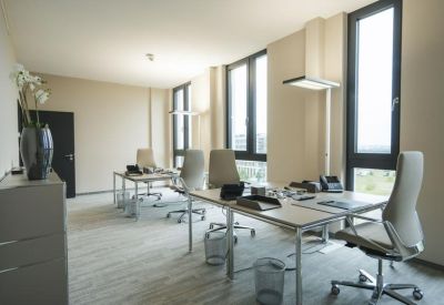 Open-plan office with multiple desks, ergonomic chairs, and large windows.