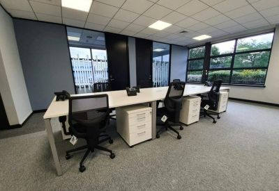 Bright workspace featuring long communal desks and large windows overlooking greenery.