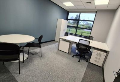 Private office suite with a round meeting table and two workstations by a window.
