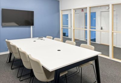 Spacious meeting room with a large white table, cream chairs, and a wall-mounted TV against a blue accent wall.