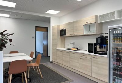Modern breakroom kitchen with light wood cabinetry and a coffee machine.