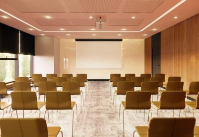 Bright auditorium-style meeting room with rows of chairs and a large projection screen.