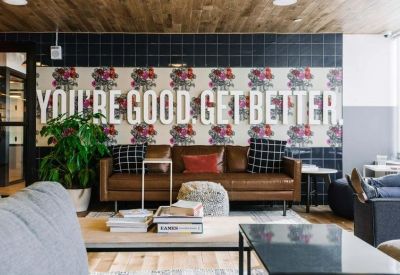 Lounge area featuring a brown leather sofa, patterned wall with motivational text, and potted plants.