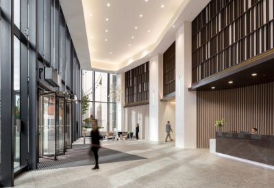 Grand building lobby with high ceilings, a dark marble reception desk, and a revolving glass door.