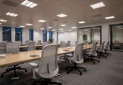 Bright open-plan workspace with rows of white mesh ergonomic chairs and light wood desks.