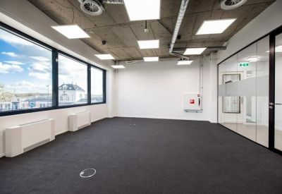 Empty modern office room with dark carpet, white walls, and industrial ceiling.