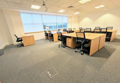Open-plan office suite with rows of wooden desks and black mesh ergonomic chairs.