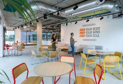 Spacious communal breakout area with colorful chairs, wooden tables, and inspirational wall art.