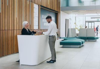 Bright reception area featuring a white desk, wood-paneled walls, and teal lounge seating.