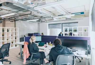 Open-plan office with white desks, purple privacy screens, and exposed ceiling ductwork.