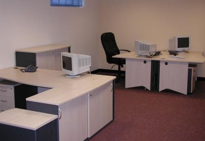 Spacious open-plan office area with several light-colored desks and CRT monitors.