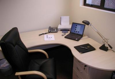 Private corner office suite with a curved wooden desk, black leather chair, and laptop.