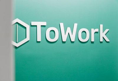 The 3D logo for ToWork mounted on a vibrant teal-colored feature wall.