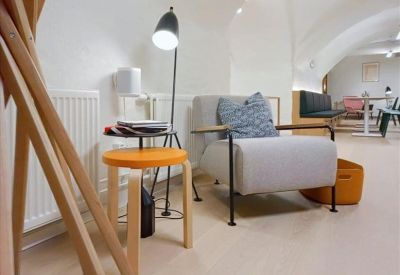 Lounge area with a grey armchair, wooden stool, and arched architecture.
