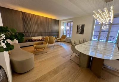 Spacious lounge area featuring a long marble table, tan armchairs, and a wall-mounted fireplace.
