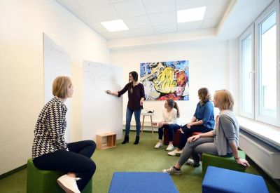 Meeting room with people collaborating around a whiteboard and colorful seating.