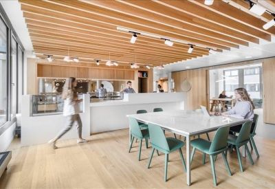 Communal coworking area with a wooden slat ceiling, white tables, and green chairs.