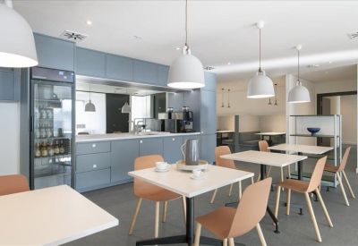 Communal kitchen and dining area with blue cabinetry and warm wood-toned chairs.