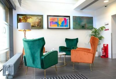 Reception waiting area featuring vibrant green and orange velvet wingback chairs and colorful artwork.