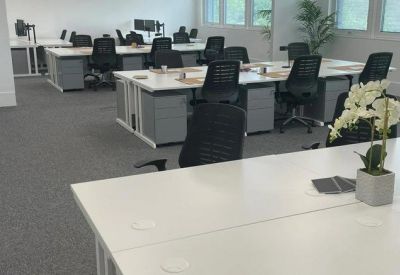 Spacious open-plan office with rows of white desks and ergonomic black chairs.