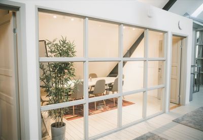 Meeting room with a white table and grey chairs behind a glass wall.