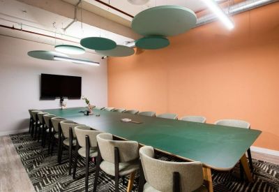 Long green boardroom table in a bright meeting room with orange feature walls.