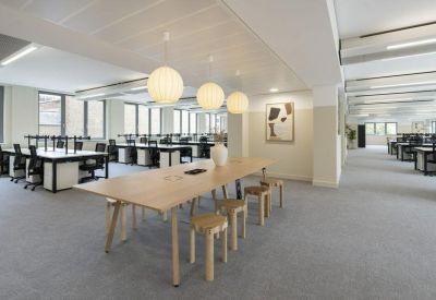 Modern open-plan office with communal wooden table and spherical pendant lights.