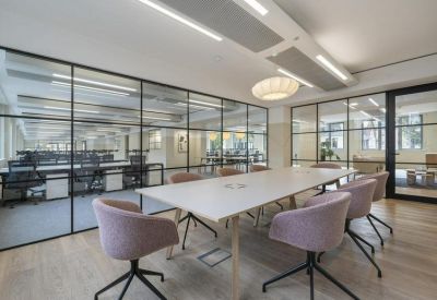 Professional meeting room with light pink chairs and glass walls overlooking desks.