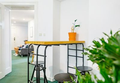 High wooden bar table with black stools located in a bright communal area.