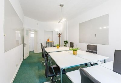 Bright open-plan office with white desks, black ergonomic chairs, and wall-mounted whiteboards.