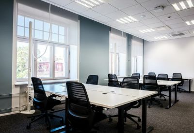 Meeting area with two large white tables and black mesh ergonomic chairs.