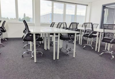 Bright coworking space with multiple white desks and black mesh chairs.