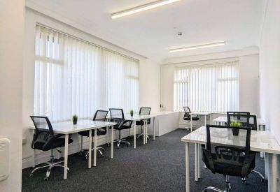 Modern office room with white desks, black chairs, and large windows with vertical blinds.