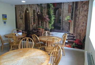 Communal dining area with wooden tables and a vibrant Italian street scene mural.