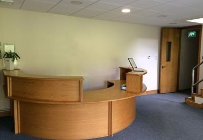 Curved wooden reception desk in a bright lobby with blue carpeting.
