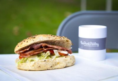 A fresh bacon and salad sandwich next to a branded coffee cup on a white table.