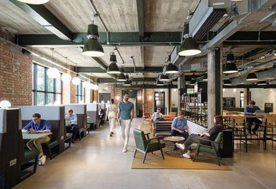 Large open-plan coworking space with industrial lighting, exposed concrete ceilings, and various seating options.