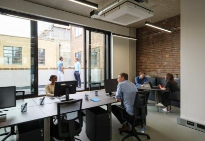 Bright office space with long desks, ergonomic chairs, and large windows overlooking a terrace.