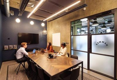 Modern meeting room featuring a wooden herringbone table, dark blue accent wall, and glass partitions.