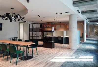 Spacious communal breakout area with a long dining table, dark green chairs, and a creative light fixture.