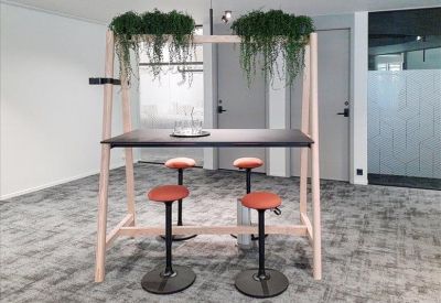 High-top wooden meeting table with four orange stools topped by hanging greenery.
