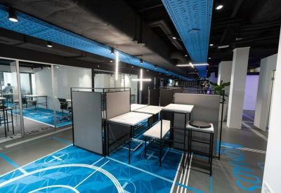 Open-plan workspace with semi-private desk pods and blue branded flooring.
