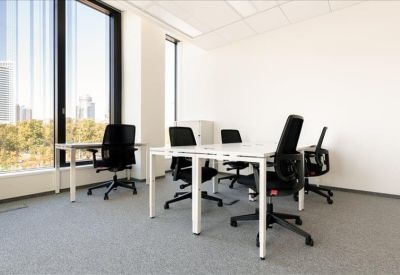 Bright corner office with white desks, black ergonomic chairs, and large windows.