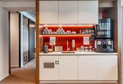 Sleek office kitchenette with white cabinetry, coffee machine, and red backsplash.