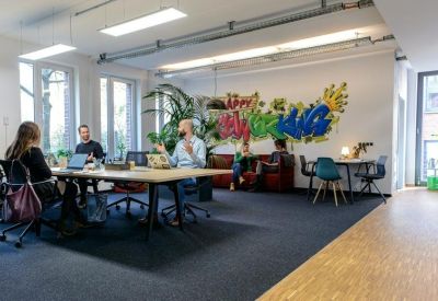 Open-plan coworking office with a large graffiti mural and long communal tables.
