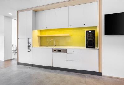 Modern communal kitchen area with white cabinetry and a bright yellow backsplash.