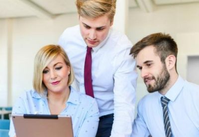 Three colleagues in business attire reviewing a document together in a bright, modern workspace.